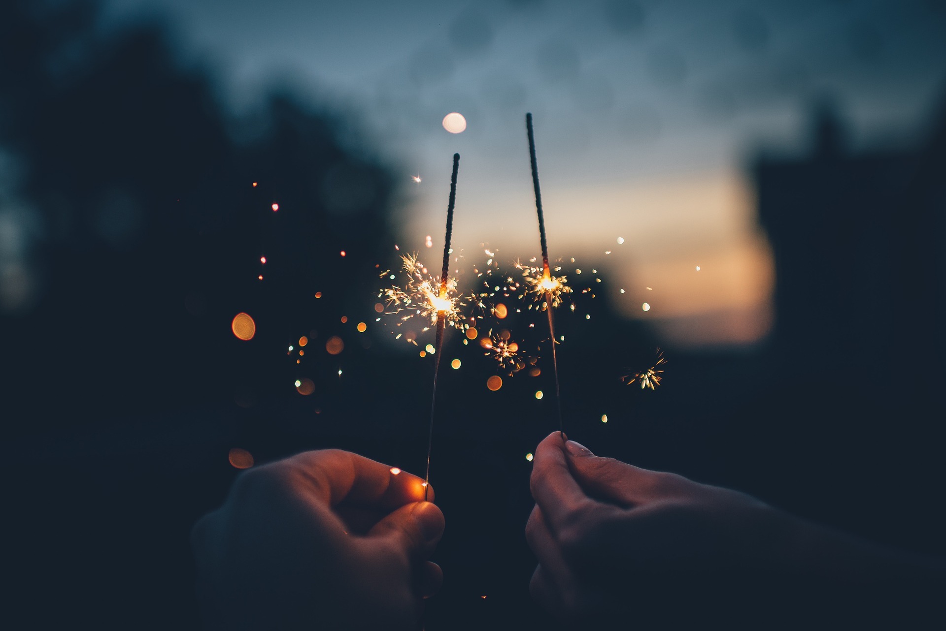 Two hands holding lighted sparklers in front of a blurred background as a symbol for the turn of the year
