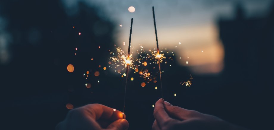 Two hands holding lighted sparklers in front of a blurred background as a symbol for the turn of the year