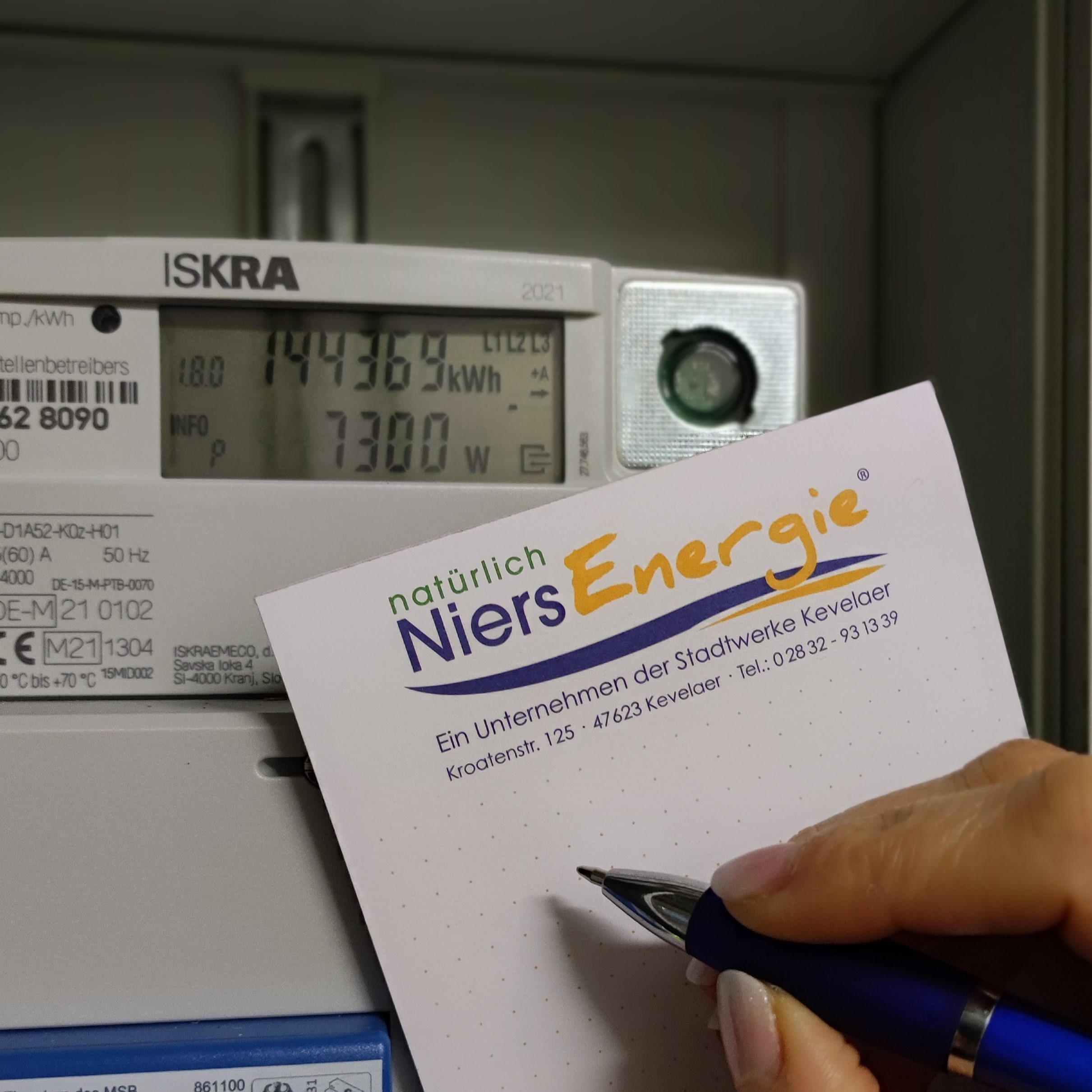 A hand makes a note of a meter reading on a pad - an electricity meter can be seen in the background.