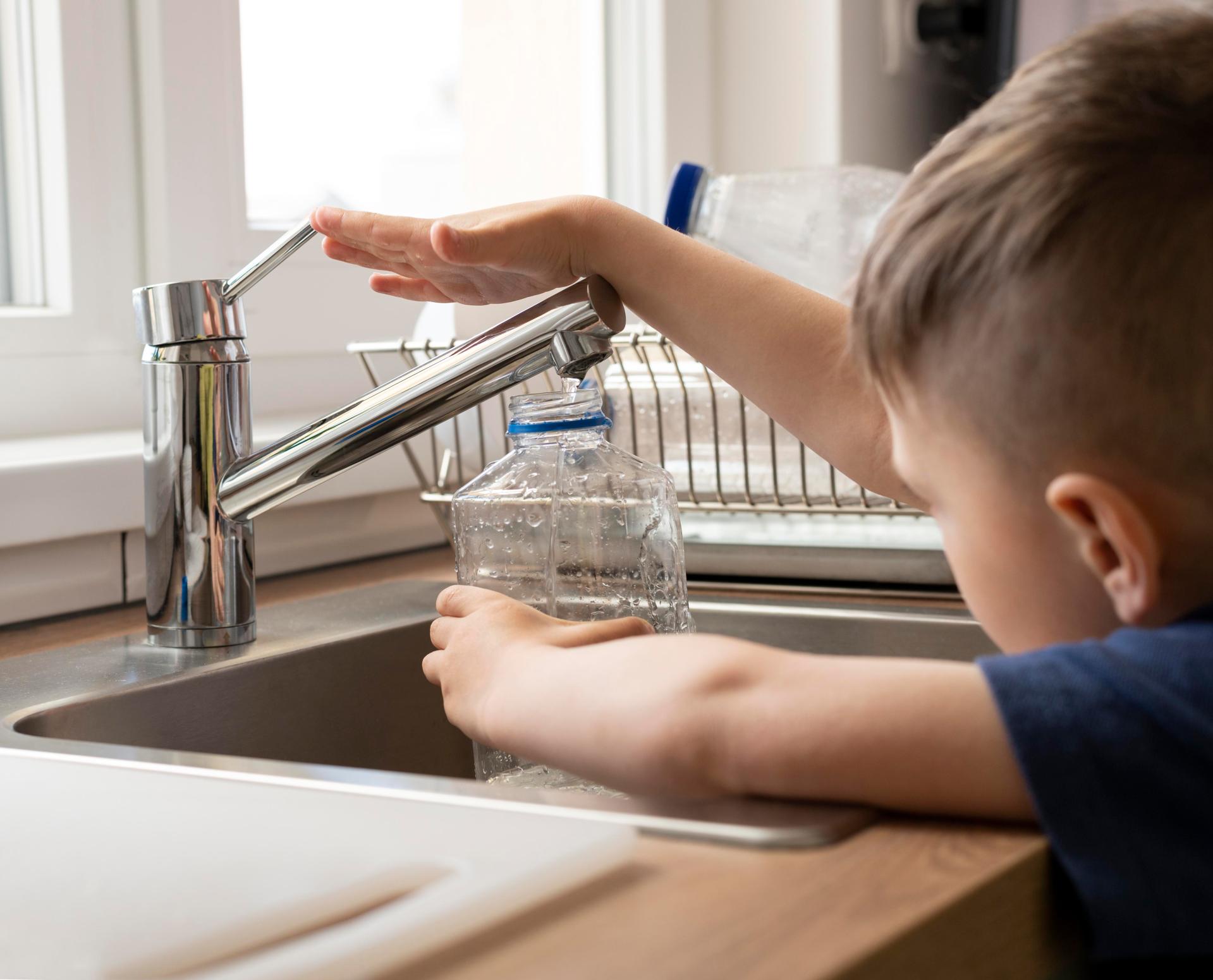 A boy fills a water bottle at the tap.