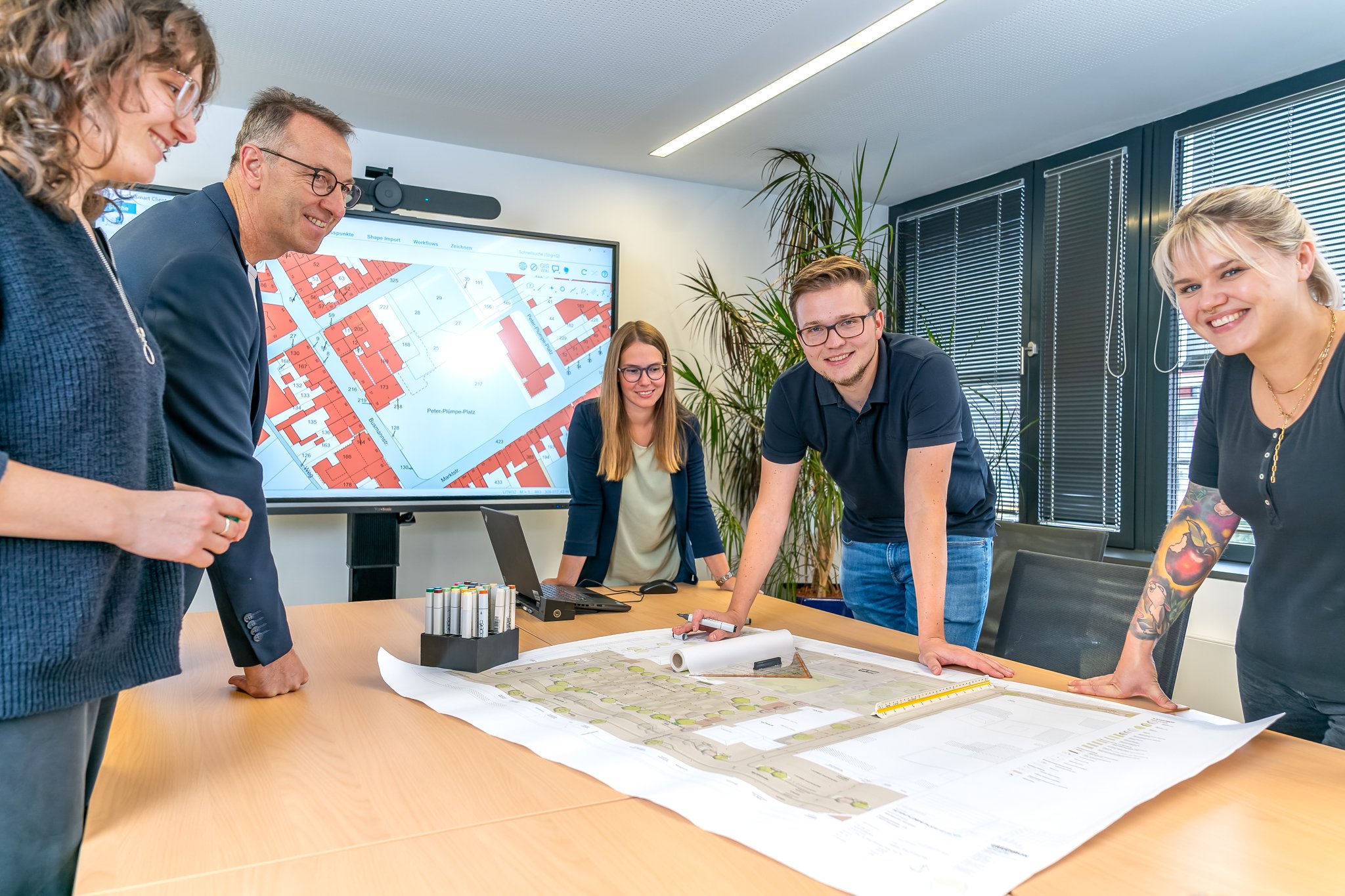 Auf dem Bild ist eine Personengruppe zu sehen, die sich über einen auf einem Tisch liegenden Plan beugt.