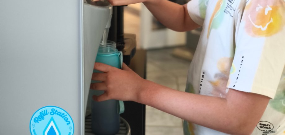 Ein Kind füllt an einem Wasserspender seine Trinkfalsche auf. 