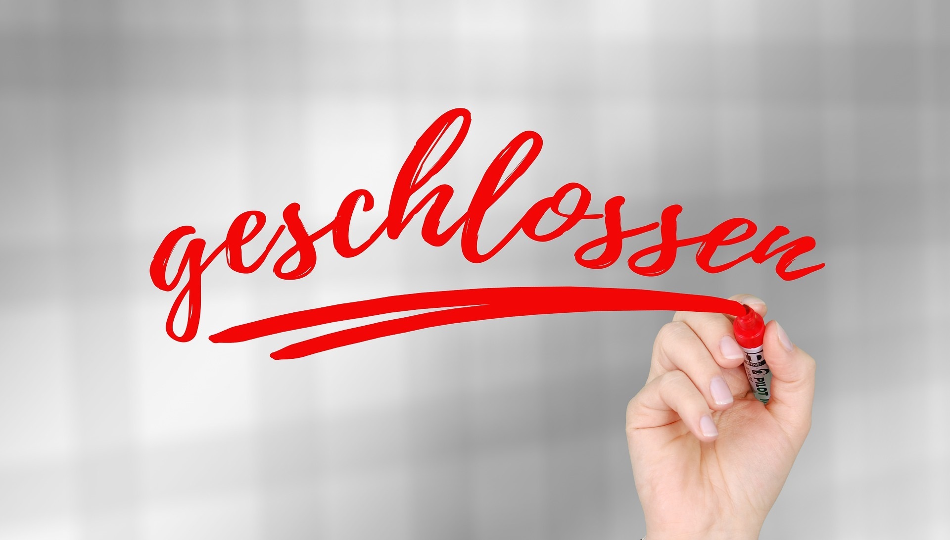 Eine Hand schreibt das Wort "geschlossen"