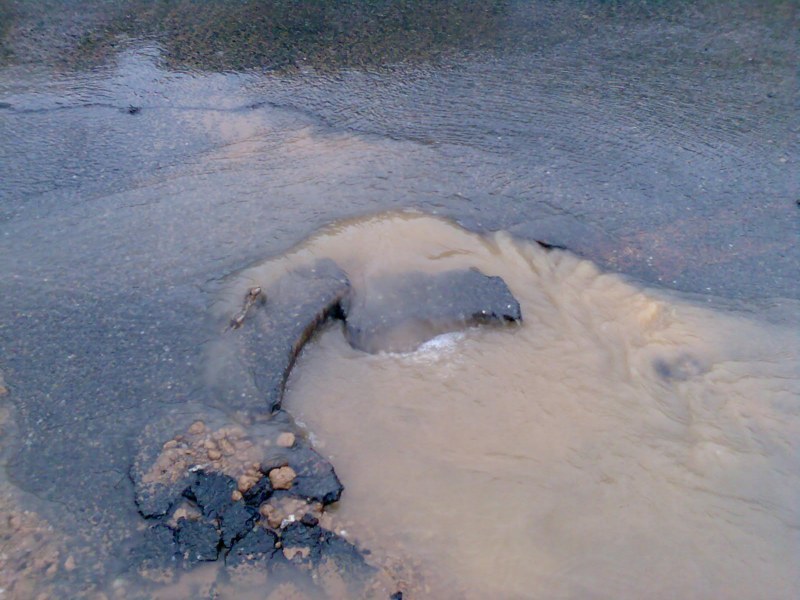 Ein Loch in einer Asphaltdecke, aus dem Wasser austritt