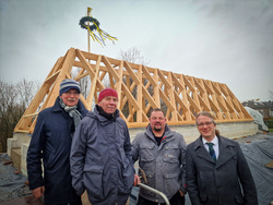 Vier Männer stehen vor einer Holzkonstruktion, aus der ein Richtkranz ragt. 