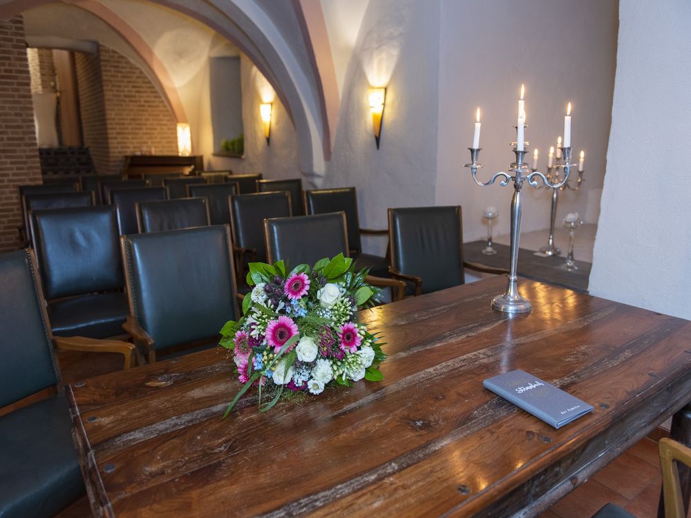 Tisch mit Blumen, Kerzenständer und Bestuhlung.