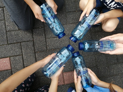 Kinderhände halten blaue Trinkflaschen kreisförmig in die Kamera.